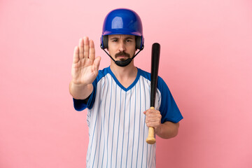 Young caucasian man playing baseball isolated on pink background making stop gesture