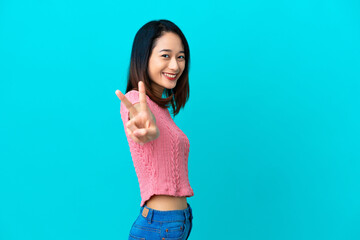 Young Vietnamese woman isolated on blue background smiling and showing victory sign