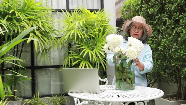 Elderly women takes thatIn the morning in the garden, decorating the white artificial flowers in a dozen glasses that she studied the technique according to the online slide on the lapot.