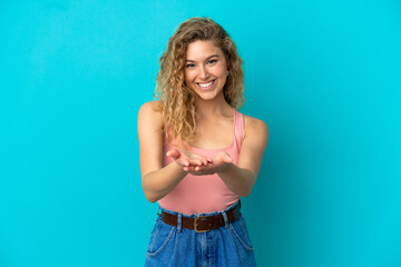 Young blonde woman isolated on blue background holding copyspace imaginary on the palm to insert an ad