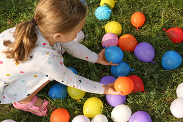 Obraz premium Little girl with water bombs on green grass, above view