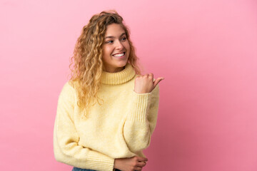 Young blonde woman isolated on pink background pointing to the side to present a product