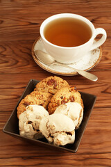 Oatmeal cookies with walnuts and raisins, meringue cookies with hazelnuts in a square bowl and a cup of green tea on a wooden table. Closeup