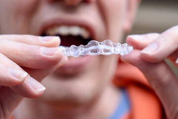 Man holding put on invisible braces. Orthodontic dental braces teeth straighteners. Gap between...