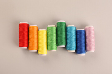 Different colorful sewing threads on light grey background, flat lay