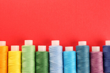 Different colorful sewing threads on red background, flat lay. Space for text
