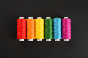 Different colorful sewing threads on black background, flat lay