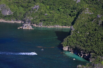 aerial view of people paddling sup standup paddle boards in calm waters with a Bangka boat and beaches and mountains in the background. Philippines