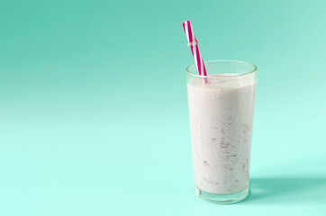 Milkshake in a transparent container with pieces of natural berries and a red tube of kopi space. Cocktail of ice cream, milk and berries on a colored background