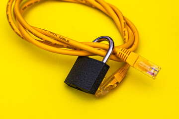 yellow internet cable twisted into a ring and a closed lock on a yellow background information protection concept