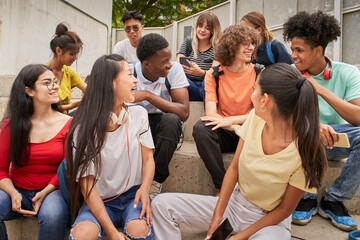 Multi-ethnic group of happy students on a break. Young people laugh sitting on the stairs of the high school.