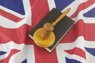 Wooden judge gavel with legal book on UK flag. United Kingdom court concept.