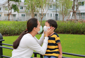 Family Asian mom wearing protective face mask for her son in the public garden during coronavirus and flu outbreak