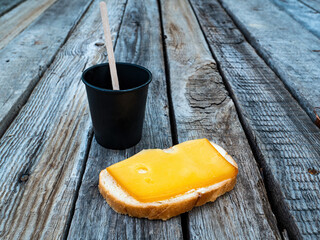 Hard cheese sandwich and a cup of coffee on a wooden table. Hard cheese. Butter. White bread. Cardboard coffee cup. Wooden table. Morning breakfast. Food intake. Street Cafe.