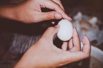 Closeup of woman's hands peeling off shell from boiled egg. Selective focus. 