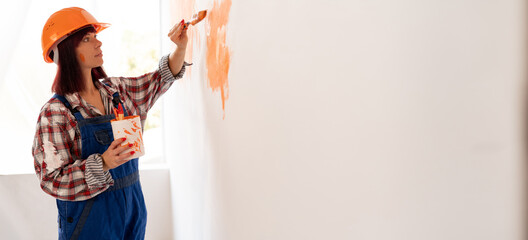 A girl in protective paint makes repairs at home, paints the wall with a brush with orange paint. Renovation work in the room. Home renovation concept
