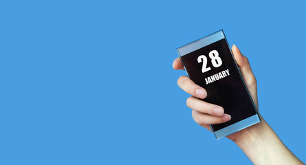 january 28. 28th day of the month, calendar date.Woman's hand holds mobile phone with blank screen on blue isolated background.Winter month, day of the year concept