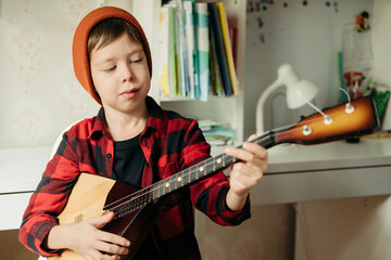 boy in a red hat and a plaid shirt plays the balalaika. Handsome boy holding his guitar. Music...
