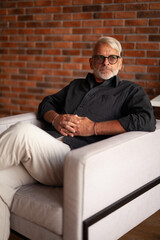 A man sitting in an armchair. The gray-haired man with glasses. Self-confident person.