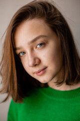 portrait of a slender teenage girl in a green sweater in natural light against a white brick wall. natural beauty, no makeup. problematic skin. space for text. High quality photo