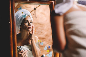 Home beauty care make over adult woman applying face cream anti age in bathroom looking on a mirror...