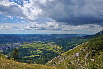 Beautiful view from the mountains towards the valley and the sea in the background. Rainy clouds in the blue sky. Vipava, Slovenia.