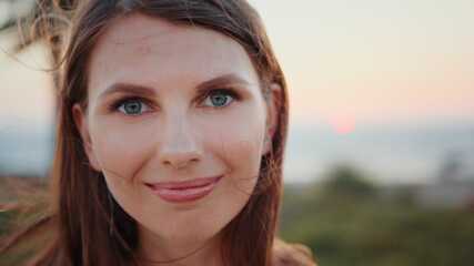 Close up portrait of stunning young woman with long brown hair and blue eyes posing on ocean beach. Sporty female relaxation during evening training on fresh air.