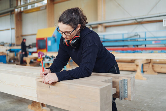 Female carpenter in an industrial factory measuring a beam