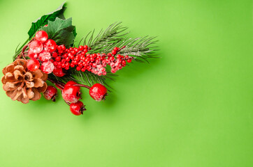 Christmas decor on a green background. A branch of a Christmas tree with decorations, red berries, cones. New Year's composition. space for text