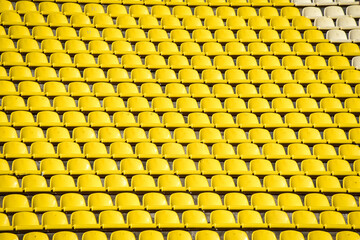 lots of rows with yellow seats for people on the football field in the summer