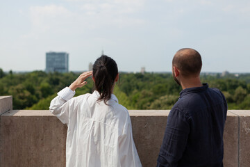 Happy married couple looking at metropolitan city view standing on tower rooftop celebrating relationship anniversary. Panoramic skyline from tower observation point. Landscape with urban buildings