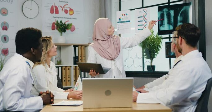 Attractive confident qualified arabian female doctor in hijab explaining results of x-ray diagnostic for attantive skilled diverse male and female colleagues during joint council