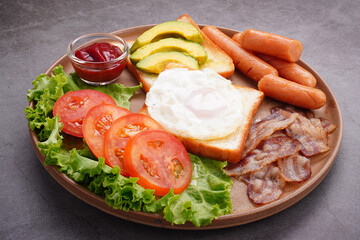 European breakfast toast eggs bacon  ​​sliced ​​tomatoeswith hot dog and vegetables in a round plate.