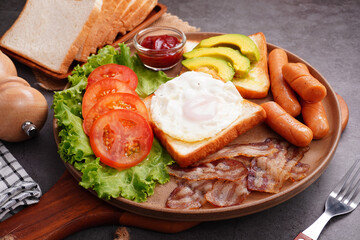 European breakfast toast eggs bacon  ​​sliced ​​tomatoeswith hot dog and vegetables in a round plate.