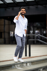 Handsome young indian businessman walking down on the stairs while talking on his phone