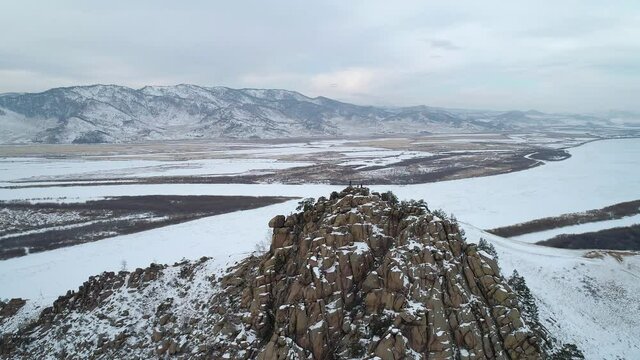 Aerial orbital shot of a rocky mountain peak covered with snow, people on the top and the valley.
