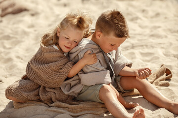 Blond haired brother and sister in cozy knit earth toned clothes playing with sand and showing true...