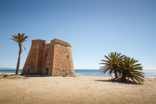 South and west facades of the Torre de Macenas next to palm trees and the beach in Mojacar, Almer&iacute;a, Spain.