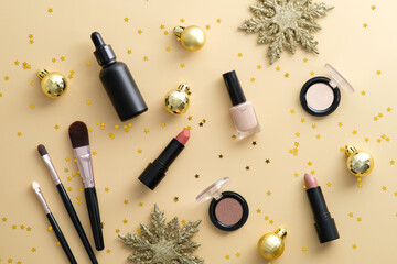 Makeup products with golden Christmas balls decorations and confetti on pastel beige background.