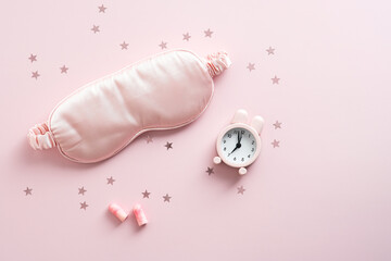Sleep mask, earplugs, alarm clock on pastel pink background. Treatments for Insomnia concept. Flat lay, top view