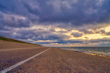 Landscape, seascape sunset on the coast of Huisduinen. The detailed road with white stripe leads to infinity. Colorful landscape  with street, long road,end point, postcard, greeting card
