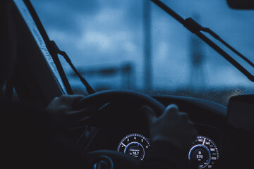 Driver's hands on wheel and city nightlife during rain