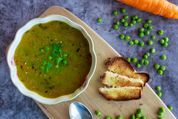 Homemade pea soup served with toasted bread or croutons. Green split pea soup rich in flavors, vegetables, herbs and healthy ingredients. Tasty soup for winter in a decorative bowl on a wooden board.