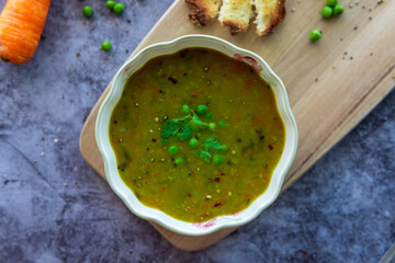 Homemade pea soup served with toasted bread or croutons. Green split pea soup rich in flavors, vegetables, herbs and healthy ingredients. Tasty soup for winter in a decorative bowl on a wooden board.