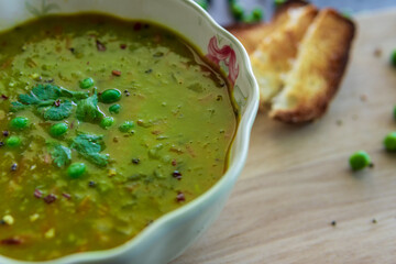 Homemade pea soup served with toasted bread or croutons. Green split pea soup rich in flavors, vegetables, herbs and healthy ingredients. Tasty soup for winter in a decorative bowl on a wooden board.