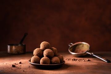 Tasty dark chocolate truffles with cocoa dusting on a brown background