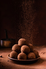 Tasty dark chocolate truffles with cocoa dusting on a brown background - 463235710