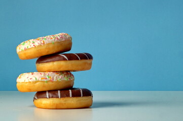 An uneven turret of four delicious fresh donuts sprinkled with different colors and with chocolate. Donuts only leash touch each other with one edge