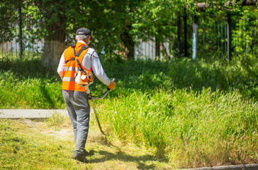 Lawn mower at work, a working man mows high grass cares for gozon. Grass-cutter closeup with copy space and space for text.