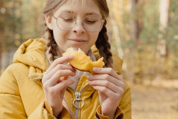 Closeup girl in glasses and yellow jacket eat pumpkin. Outdoor picnic. Little helper in preparation...
